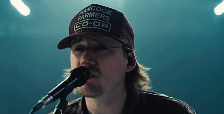 A man with a brown baseball hat singing into a microphone.